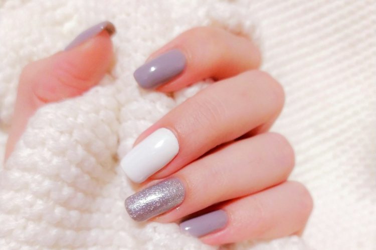 Short nails for winter in mauve and glitter holding a white knit sweater